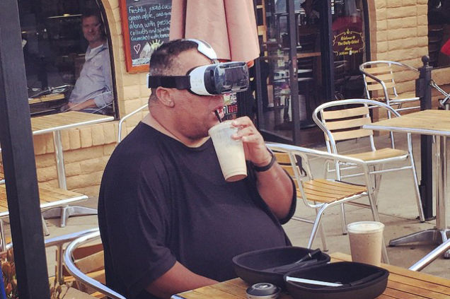 The camera can capture some fantastic moments IV - Page 133 - Photography & Video - PistonHeads - In the image, an overweight man is seated at a restaurant table, seemingly engaged in a meal. He is wearing a shirt and has a bowl of food in front of him. His face is hidden behind a large black camera, which he's holding close to his eyes in an unusual fashion. Around him, there are other chairs and tables, suggesting a public dining establishment. The overall scene indicates that the man might be using the camera to digitally enhance or document his meal, perhaps for a video or an online review.