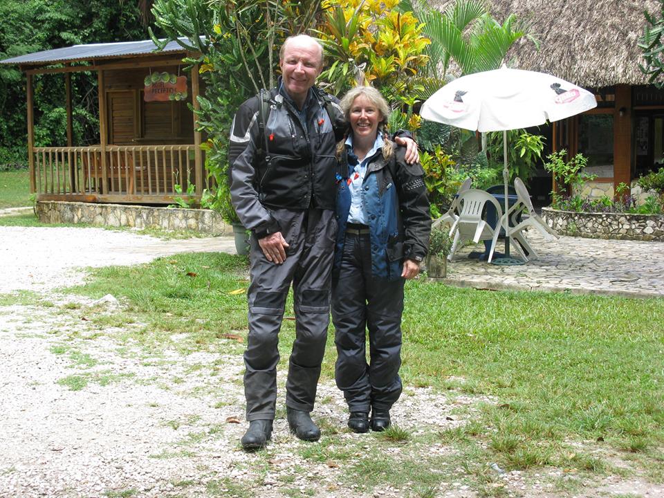 Lost your camera in Spain recently? - Page 1 - Biker Banter - PistonHeads - In the image, an older man and woman are the main subjects, standing on a gravel path in an outdoor setting. Both individuals are dressed in casual attire complemented by protective gear, suggesting a readiness for some form of outdoor activity or exploration. The man has a white beard, and they both appear to be posing for the photo. In the background, partially obscured by the couple, is a hut-like structure and an umbrella offering shade to the area. The man and woman seem to be looking towards the camera, and the atmosphere suggests a leisurely trip or adventure.