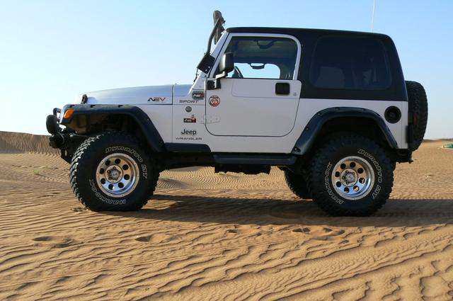 lift kits + big wheels: effect / addtional strain? - Page 2 - Off Road - PistonHeads - This image features a black and white Jeep parked on a sandy surface. The vehicle is positioned facing towards the right of the photo, highlighting its front and side profile. The Jeep's tire tracks and the driage suggest that it has recently traveled over the sand. There is a clear blue sky overhead, indicating a sunny day. The overall setting appears to be in a desert-like environment.