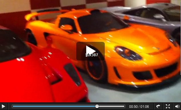 Garage Poulters Mates Pistonheads Ian Twitter - The image features two sports cars parked next to each other. One is a vibrant orange, and the other has a vivid red finish. The cars are parked inside what appears to be a garage or a showroom. The interior has a checkered pattern, the side mirrors are visible, and there's a small play button overlaid on the image, suggesting an autoplay or pause function for a video recording.