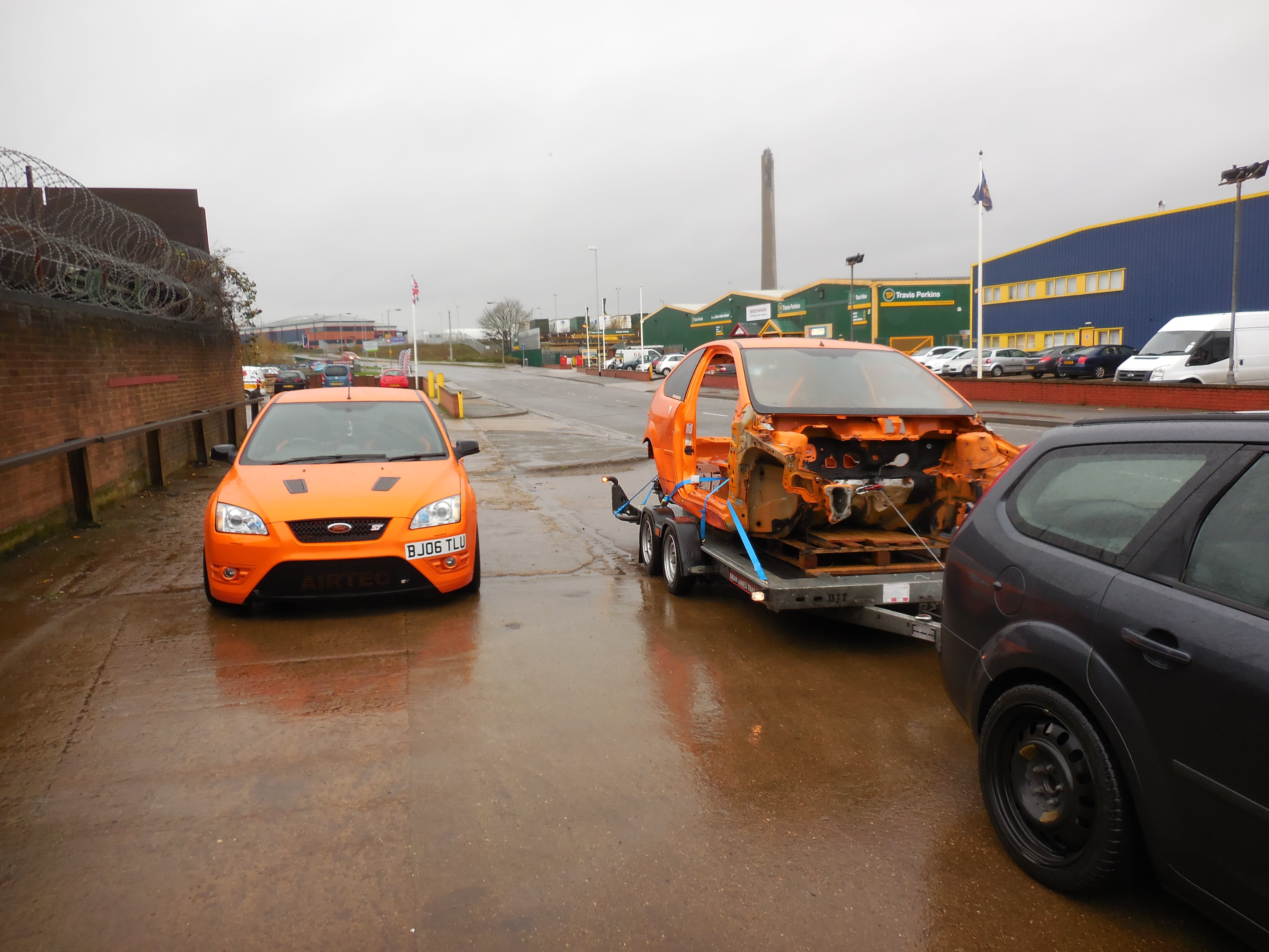 Ford Focus Mk2 [ST] Estate Sleeper - Build Thread - Page 23 - Readers' Cars - PistonHeads - The image showcases a scene of urban decay, featuring several abandoned and dilapidated vehicles. A prominent orange car sits in the foreground, exuding an aura of decay and neglect. Behind it, a black SUV stands out against the desolate setting, adding a touch of contrast to the scene. The vehicles are parked on a lot, surrounded by the remnants of a once-thriving industrial area. The large brick building in the background, now overgrown, bears witness to the passage of time and the transformation of the cityscape. The cars, despite their seemingly broken condition, still retain a sense of purpose and functionality. The overall image paints a picture of urban decline, a testament to the transience of city life.