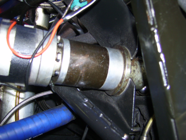 Clubsport Pistonheads Installation Reverse - The image provides a close-up view of the engine bay of a vehicle. The red and black wires are prominently featured, weaving their way through the space. Notably, there's a metallic hose or pipe which appears to be made of steel, perhaps a part of the vehicle's cooling system given its cylindrical shape. The engine bay itself is a complex network of various metal parts, hinting at the intricate nature of a vehicle's engine. The overall setting suggests a moment of mechanical curiosity or repair.