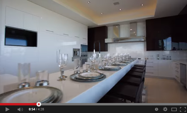 A kitchen with a table and chairs and a table - Pistonheads - The image depicts a luxurious and modern kitchen. The kitchen features white cabinets and gray countertops, creating a sleek and clean aestethic. On the counter, there are several tall wine glasses and plates, suggesting a formal dining setup or preparation for a special event. The focal point of the scene is an island in the center with a row of built-in wine glasses for six people, implying a sense of grandeur and elegance. The kitchen is well-lit, enhancing the bright and white color scheme.