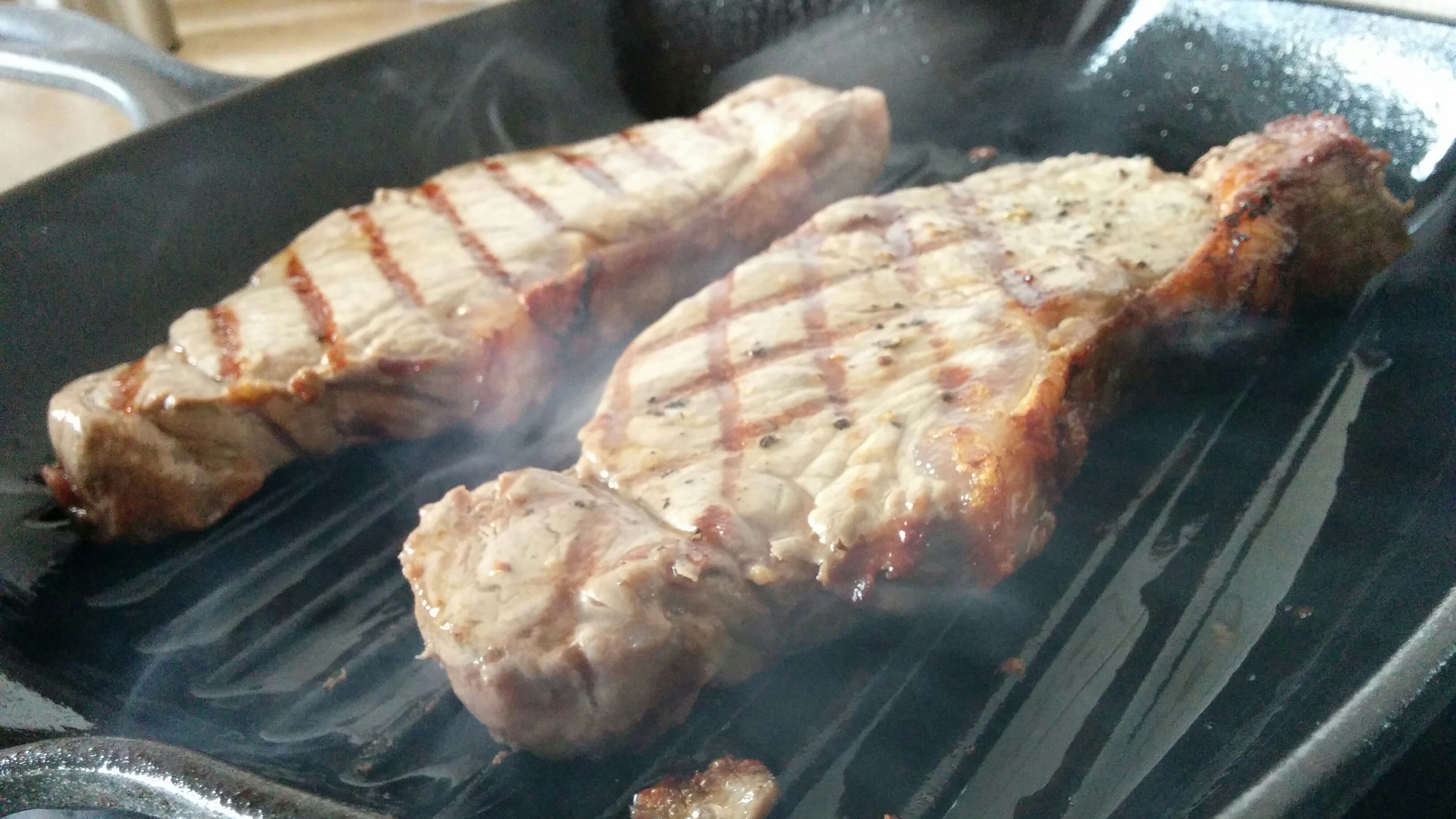 THE  STEAK THREAD, served a la Man. - Page 14 - Food, Drink & Restaurants - PistonHeads - The image shows a close-up view of three steaks, likely slices, sizzling on a hot surface. The steaks have a robust pink hue, suggesting they are slightly undercooked, as they are intended to be medium-rare. They display a grilled exterior with visible grill marks. The surface they are cooked on appears to be a griddle or a skillet, which also has visible fat dripping onto it. The image is slightly blurred, especially around the edges, making it challenging to discern details outside the immediate vicinity of the steaks.