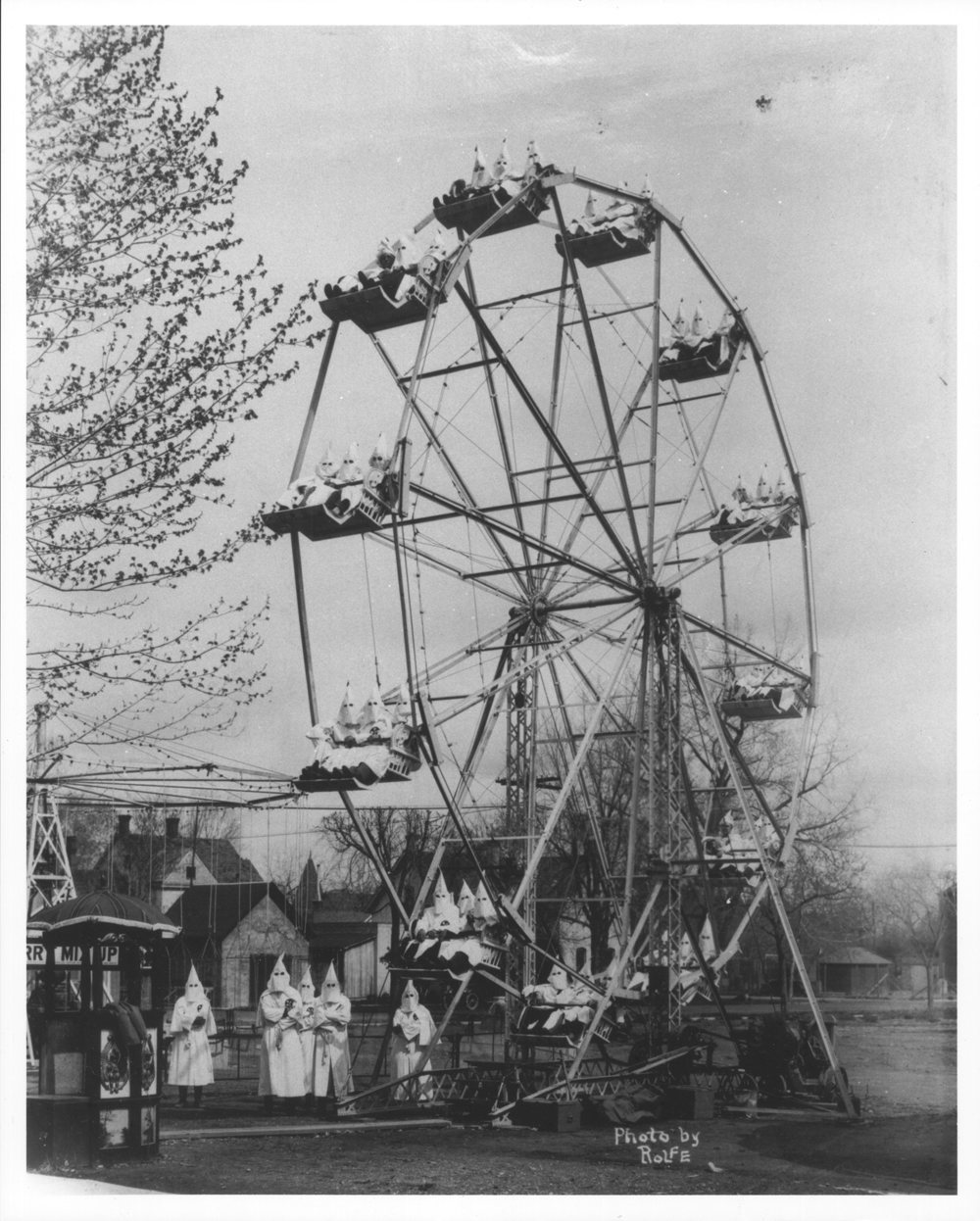 The camera can capture some fantastic moments IV - Page 483 - Photography & Video - PistonHeads - The image shows a vintage black and white photograph of an amusement park carousel. It features a large wooden structure with a merry-go-round on top, adorned with several people sitting in the seats. On this carousel, there are numerous figures dressed as Ku Klux Klan members, adding to its antiquated and controversial nature. The background shows the silhouette of trees under a clear sky, suggesting an outdoor setting during the day. The overall style of the image suggests it could be from the early 20th century.