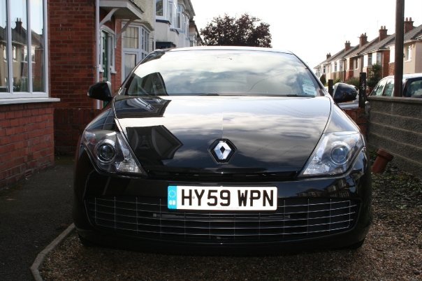 Laguna Pistonheads Coupe - The image shows a black hatchback parked on what appears to be a residential street. The car is the central focus of the image, with its sleek design and prominent badge, indicating it's a Renault vehicle. It's parked by a brick building under a cloudy sky. The license plate reads "HY59 WPN," suggesting a location or region hinted at by the acronym "WPN."