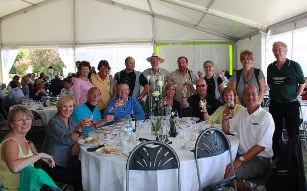 Owners Club - Page 1 - Aston Martin - PistonHeads - This image captures a friendly gathering in a large white tent, set up with numerous dining tables draped with white tablecloths. A group of people, men and women, dressed in a mix of casual and semi-formal clothing, are standing and sitting around the tables, engaging in conversation and enjoying their time. Some of them are holding up wine glasses, suggesting a celebratory occasion. A set of chairs and a mixture of drink bottles and wine glasses are visible on the tables, indicating that food and beverages are part of this social event. The people in the image appear to be enjoying themselves in a relaxed and joyful atmosphere.