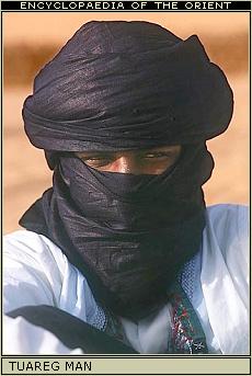 Windscreen Pistonheads Replacing Aeroscreen - The image shows a person wearing a black turban, which is wrapped tightly around the head and neck. The person appears to be of a person of Middle Eastern descent. The turban, while dark in color, has accents that suggest a cultural or traditional design. The facial features are obscured by the black fabric of the turban, leaving only the eyes and chin partially visible. The background hints at a warm, possibly desert-like environment with a hazy, overcast sky.