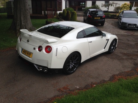 Our Cars - Page 131 - Scotland - PistonHeads - The image shows a white sports car parked on a dirt driveway. The car is positioned alongside a house with a visible front door. To the right of the frame, there is a compact black car and additional greenery. The sunny weather and lack of rain contribute to a clear view of the vehicles.