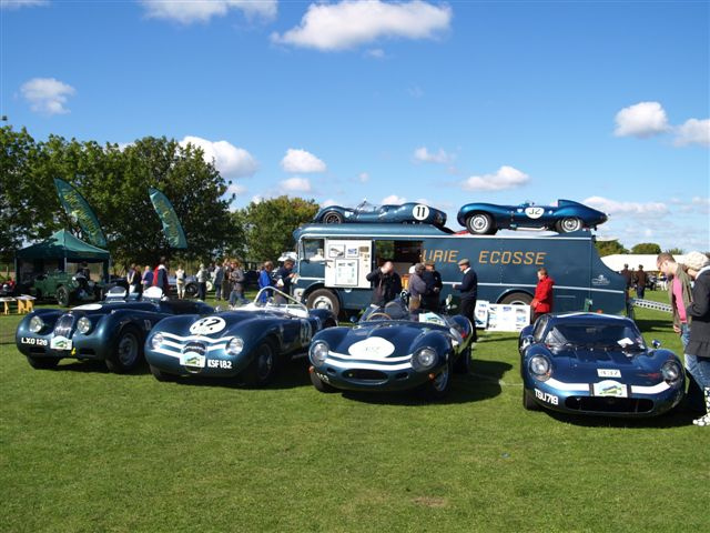 Pistonheads - The image captures a bright day at an outdoor auto show. Several antique cars, painted in various shades of blue and white, are on display on a grassy field. A unique feature is a small blue replica of a car on top of one of the cars, adding a playful touch to the event. There are numerous people scattered around the vehicles, suggesting an interesting social aspect to the gathering. In the background, a truck with more cars is parked, indicating a larger event beyond this display. A tree can be seen in the far distance, providing a natural contrast to the event.