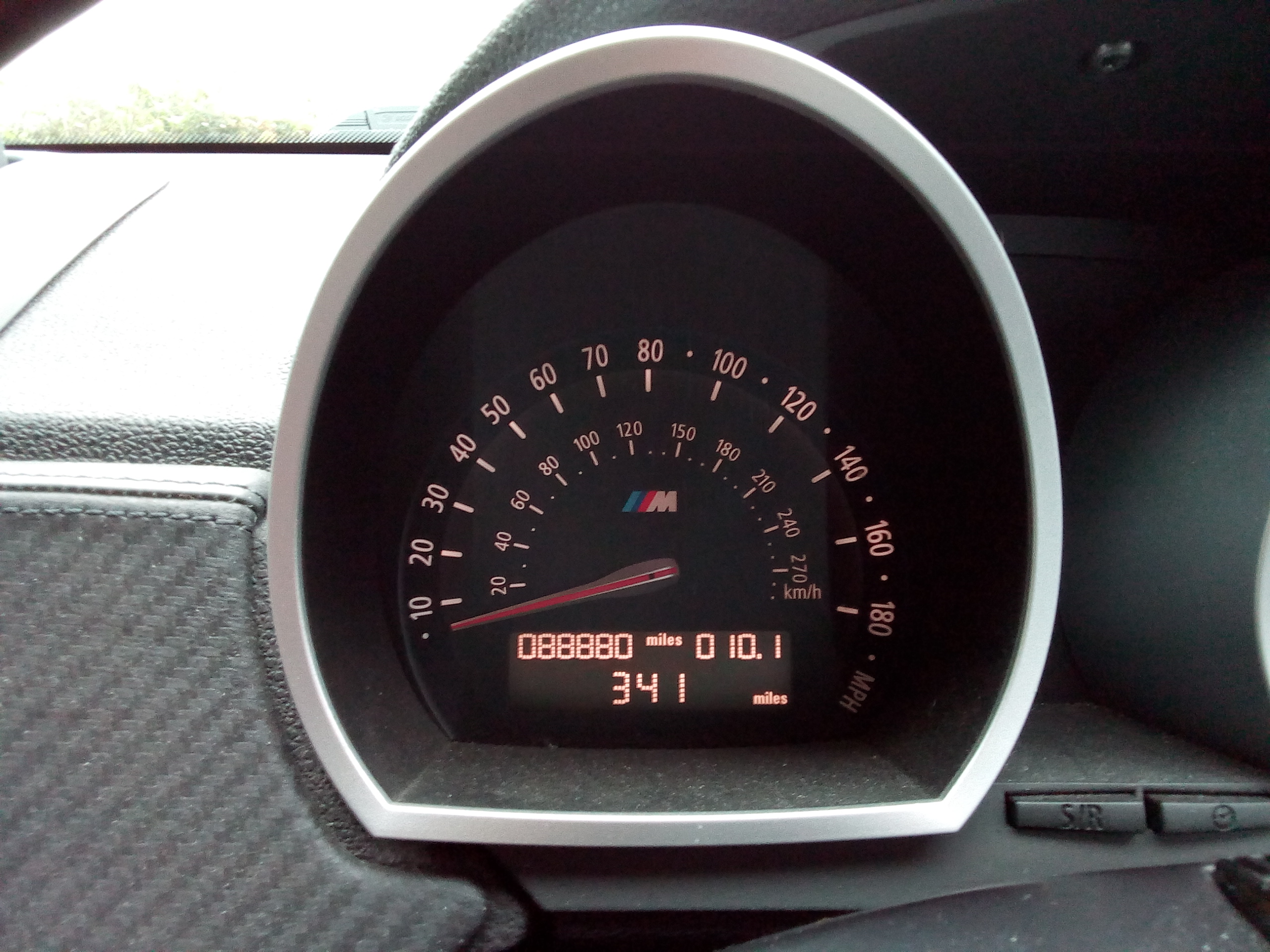 Pistonheads - The image shows a close-up of the instrument panel inside a car. The panel is dominated by a speedometer, which indicates a reading of 0 km/h. Above the speedometer, there's an odometer that displays "389", and below it, a gauge for fuel level. There are also indicators for distance to empty and battery charge. The car appears to be stationary, as evidenced by the needle on the speedometer pointing straight up. The background is out of focus, drawing attention to the dashboard.