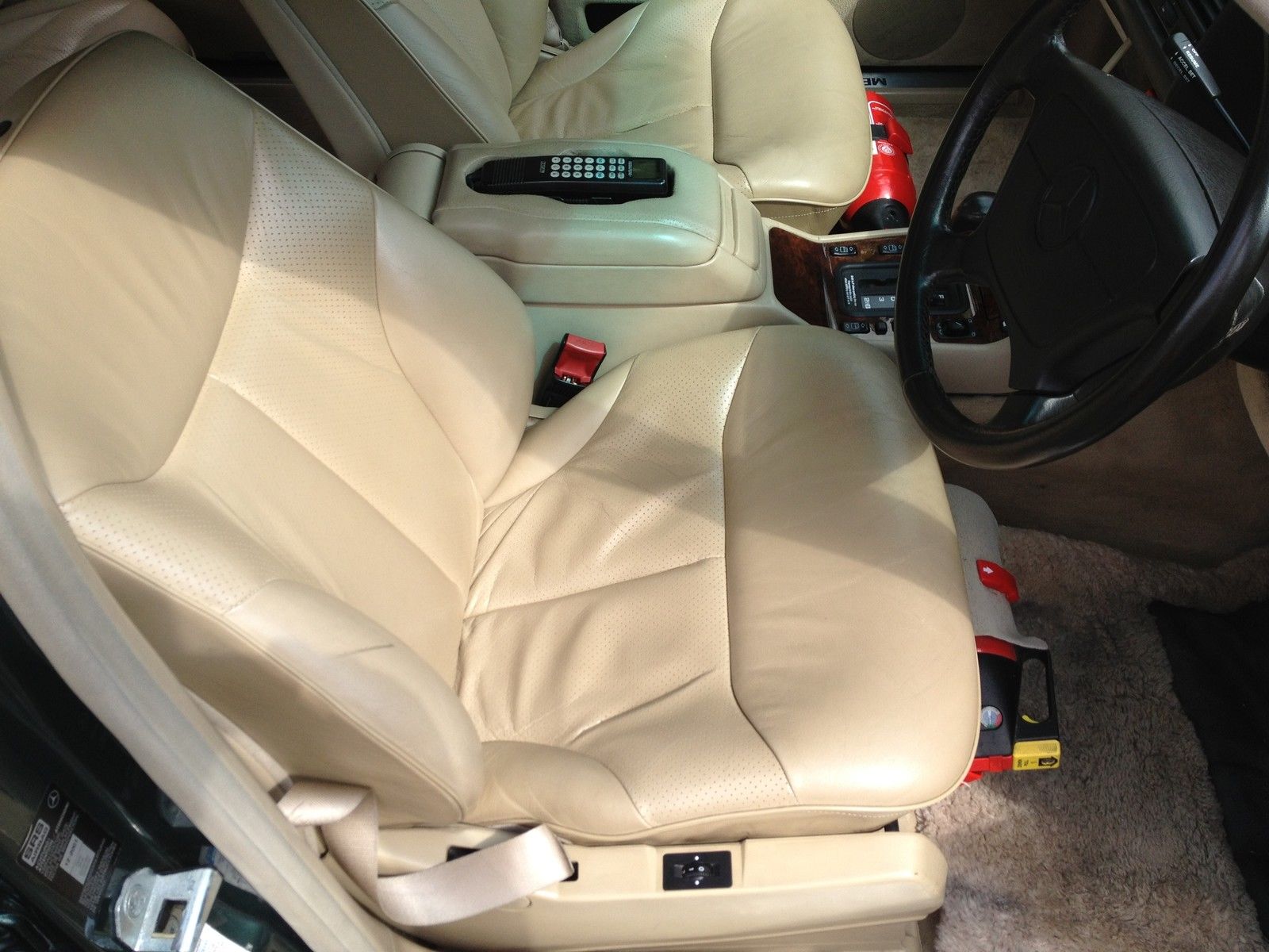 A car is parked on the side of the road - Pistonheads - The image displays the interior of a vehicle vehicle, specifically focusing on the driver's side of the cabin. The driver's seat is prominent in the foreground, featuring a tan leather upholstery. The steering wheel is in the upper right corner of the image, and the gear shift is visible to the left side of the frame. Underneath the driver's seat, there are what appear to be car accessory bags and electronics, indicating a customized setup within the vehicle. The lighting in the image suggests it is an indoor setting.