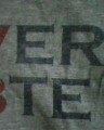 Printed by robots? - Page 1 - PH Shop - PistonHeads - The image shows a close-up view of text on a fabric, which appears to be a t-shirt based on the thread and texture. The text reads "VERA" in uppercase letters with a bold and slightly italicized font. The background behind the text is a textured fabric that might be gray, creating a subtle contrast with the darker text. The focus of the image is on the spelling of the word "VERA," with the letters clearly legible against the backdrop. The style of the image is straightforward and does not contain additional graphics or embellishments beyond the text.