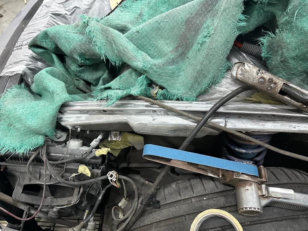 Pistonheads - The image shows a car with its hood open, revealing the engine. Various mechanical parts and wires can be seen in the engine compartment. There are two pieces of fabric draped over the car, one green and one blue, which might be protective coverings or makeshift barriers. Additionally, there appears to be a tool or instrument with a blue handle lying on the ground near the car's front end. The environment suggests an outdoor setting, possibly a driveway or garage, given the presence of what looks like a tarp on the left side.