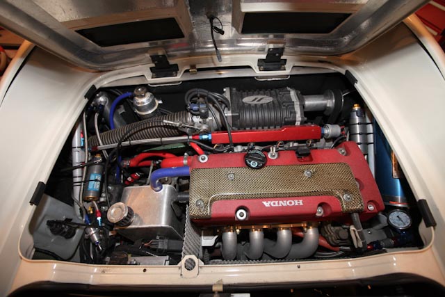 Pistonheads Lotus Elise - The image shows the engine bay of a firearm, revealing its intricate mechanical components. The engine appears to be in the process of being repaired or maintained, as the hood is slightly open and parts are scattered around. There's a visible brand name on part of the engine. A variety of wires and hoses are visible, connecting different parts of the engine. Most of the engine components are metallic and there's notable use of red as a color for parts of the engine.