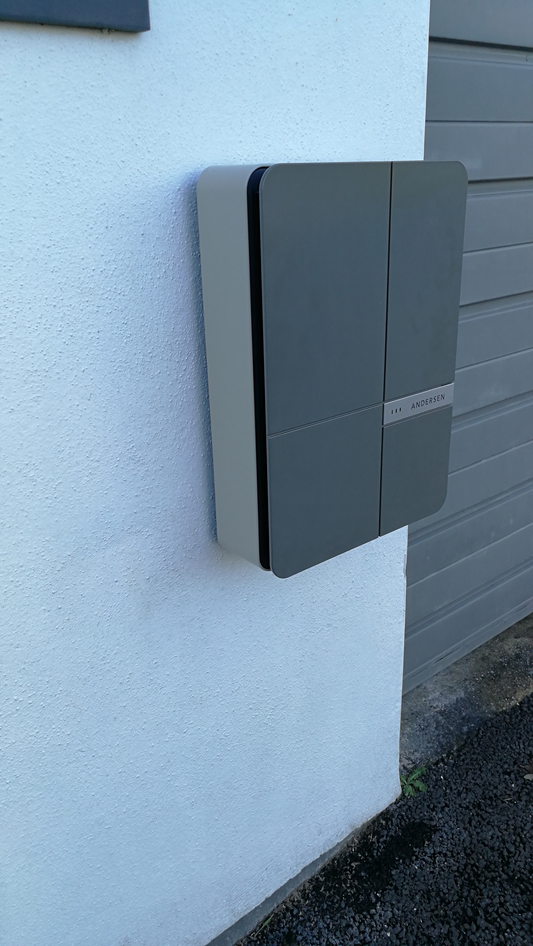 Which home charging point? - Page 3 - EV and Alternative Fuels - PistonHeads - The image depicts a utility box mounted on the wall of a building. The box is grey with some black accents, and it features two prominent vertical lines that divide the space evenly. It's a sunny day outside, as evidenced by the brightness illuminating the scene. The box appears to be an integral part of the building's infrastructure, likely housing important utilities or equipment.