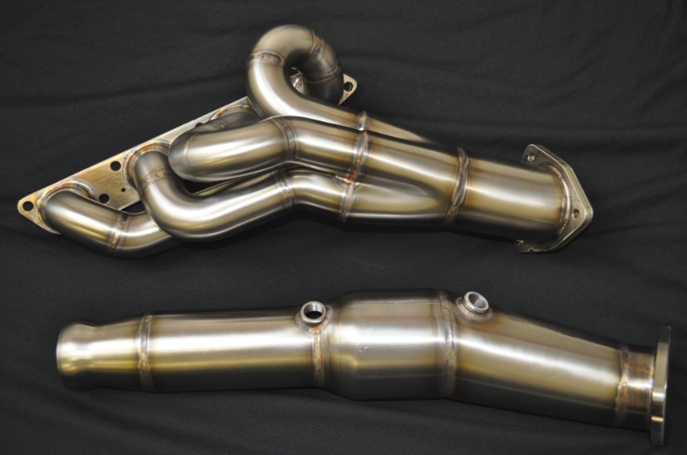 Pistonheads - The image displays a pair of automotive mufflers, which are components of a vehicle's exhaust system. The mufflers have a cylindrical shape with a metallic finish that reflects light, highlighting their shiny surface. They are positioned diagonally across the image, showing both ends of the parts. The mufflers are likely components of a performance or aftermarket car part, given their sleek design and neatly aligned silhouette.