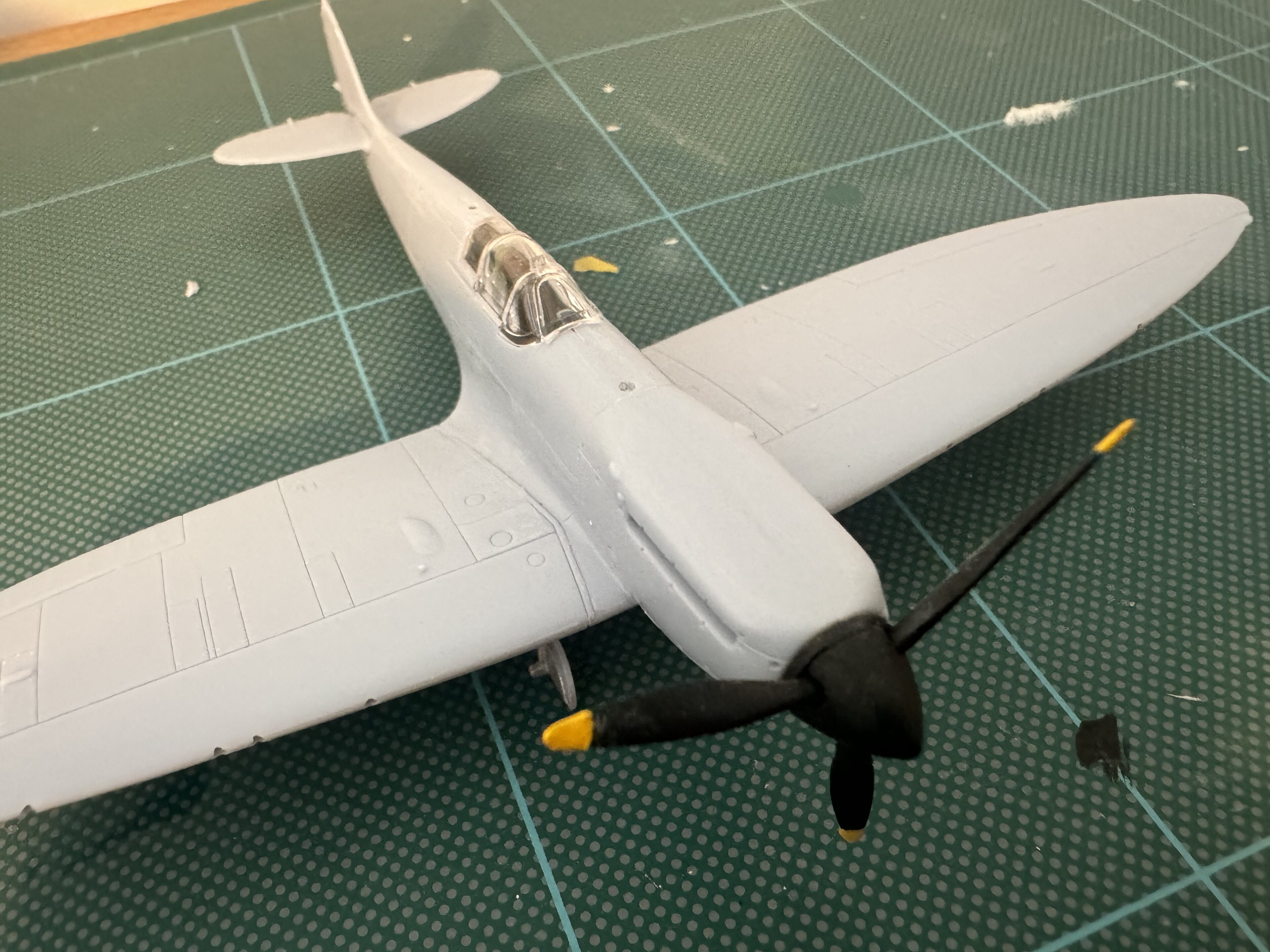 Pistonheads - This image shows a model plane, painted in white with accents of yellow and black. The model is designed to resemble an old-style biplane, featuring two sets of wings stacked one above the other. The propeller, which is at the front, has a propeller blade attached. The model airplane is placed on a tabletop surface with a grid pattern. There are no texts or people present in this image.