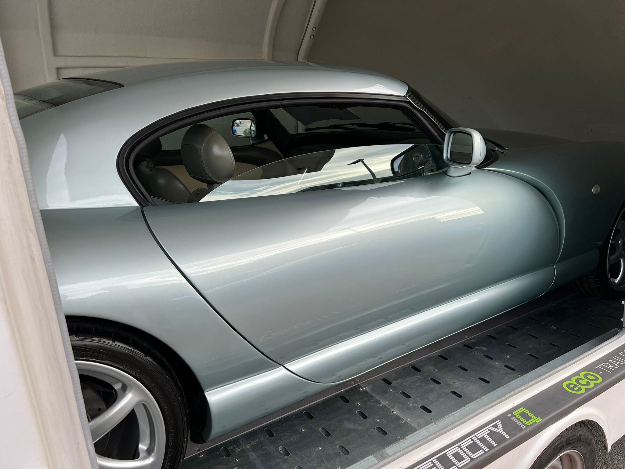 importing a Cerbera to the USA - Sept/Oct 2022 - Page 2 - TVR in USA - PistonHeads UK - The image shows a silver sports car with the hood up, parked on a ramp in what appears to be an indoor setting. It is a sunny day outside as indicated by the light shining through the windows. The car's engine compartment is exposed, suggesting maintenance or inspection might be underway. There is a handicap accessibility symbol visible near the car, indicating that this area is accessible for individuals with disabilities.