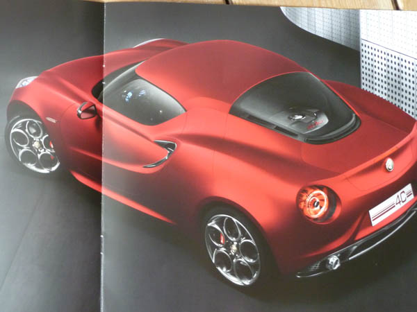 Received an Alfa 4C brochure through the post today. - Page 1 - General Gassing - PistonHeads - This is a photograph of a red convertible sports car. The car is positioned at a three-quarter angle and has a black roof panel that is lowered. Its design showcases the aerodynamic shape of the vehicle with the side edge of the hood and the front bumper seen. This is likely an advertisement or a digital rendering of the car, showcasing its sleek and sporty design.