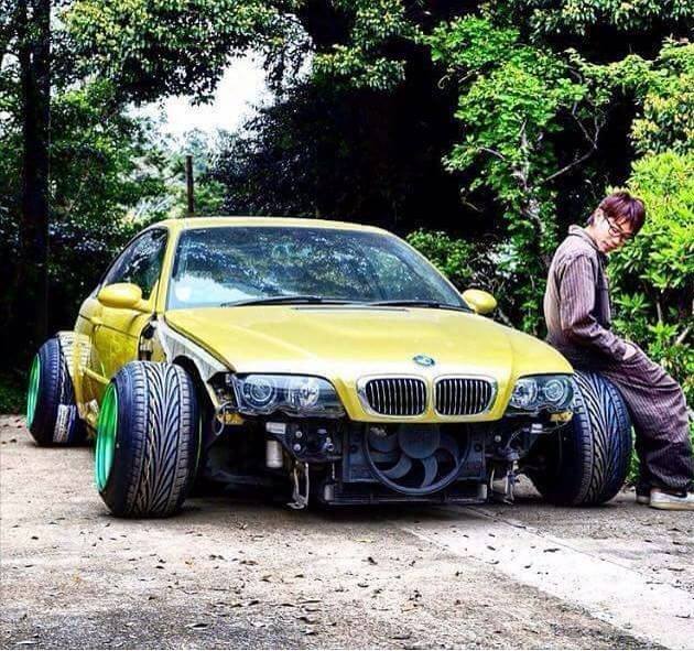 Badly modified cars thread Mk2 - Page 141 - General Gassing - PistonHeads - The image features a person leaning against a yellow three-wheeled motor car with oversized tires. The vehicle is parked in a setting that appears to be a rural or lightly wooded area, as suggested by the presence of greenery and trees around. Interestingly, the car is missing its front bumper and hood, which are not present in the image. The person appears to be pleasant, with a relaxed posture as they look towards the car. The colors in the image include the dominant yellow of the vehicle, the green of the surrounding environment, and various shades of gray in the background.