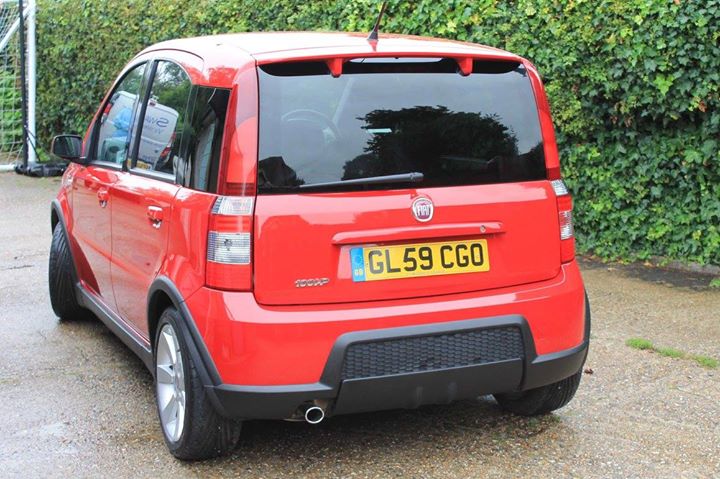 Matt's Panda 100HP - Page 1 - Readers' Cars - PistonHeads - The image presents a vibrant red Fiat Punto, a small, two-door hatchback car. The car is parked in a lot next to a lush green hedge that adds a serene backdrop to the vehicle. A yellow license plate is visible, bearing a UK registration (CL59 CGO). The car's body and windshield reflect the light, suggesting recent exposure to sunlight. The overall scene suggests a peaceful day in a landscaped parking area.