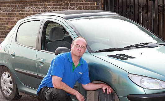 Not a very nice man - Page 1 - General Gassing - PistonHeads - The image depicts a man squatting down beside a green car. He is wearing glasses and a blue shirt. His pose suggests he may be examining or admiring the vehicle. The car appears to be compact, with a shiny exterior suggesting it could be in good condition. The man's glasses add a touch of sophistication to the scene.