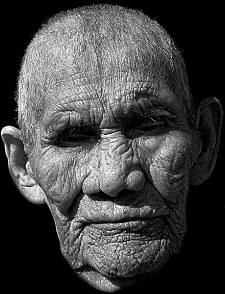 A man in a suit and tie holding a microphone - Pistonheads - The image is a close-up portrait of an elderly, bald man with wrinkled skin on his face. The man's expression is neutral with closed eyes. The most prominent features are his highly defined facial wrinkles which are accentuated by a slight shadow across the right side of his face. The contrasting skin tones and the high detail highlight the age and character of his features. The style of the photograph emphasizes the texture and contours of the subject's face, which suggests a mood of age or wisdom.