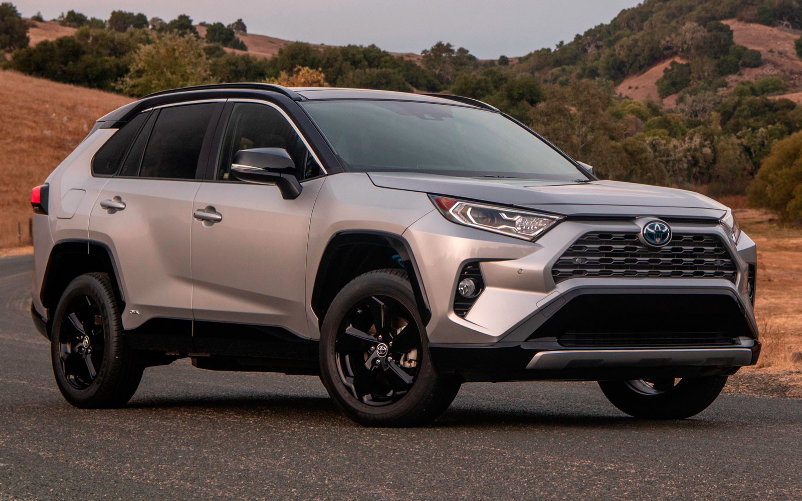 A car parked on the side of the road - Pistonheads - The image shows a silver Toyota RAV4 SUV parked on the side of a road. It is a modern vehicle with a distinct front grille and black rims. The car is positioned facing left, with a clear sky in the background suggesting it might be early morning or late afternoon. The surrounding environment indicates that the vehicle is in a rural area, possibly in the United States, given the style of the SUV and the road design.