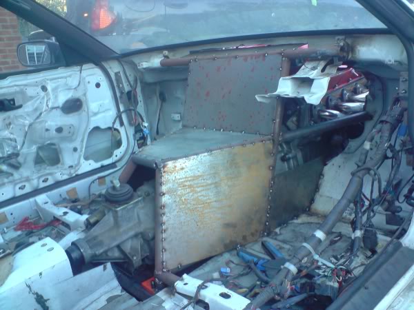 Engine Pistonheads Owner Viper - This image shows the interior of a car undergoing repairs. The dashboard is exposed and without the instrument panel, revealing the mechanics behind it. On the seat, a rusted box and loose wires indicate parts that have been removed or damaged. The interiors of other vehicles can be seen behind this one, suggesting a shared garage or repair workshop. There is no clear visual indication of a person working in the image.