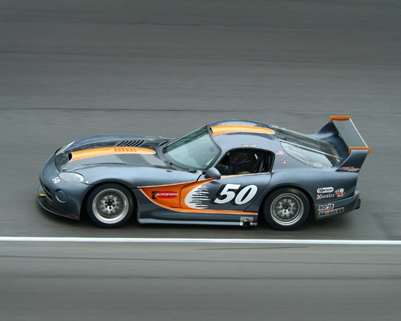 ACR style gen 1 Viper - Page 1 - Vipers - PistonHeads - This image showcases a striking black and orange racing car in action on a track. The vehicle features vibrant livery and a prominent number "50" on its hood, adding to its racing aesthetics. The backdrop is a blurred track surface, emphasizing the car's speed and movement. It is captured in a dynamic setting, conveying the thrill and intensity of competitive racing.