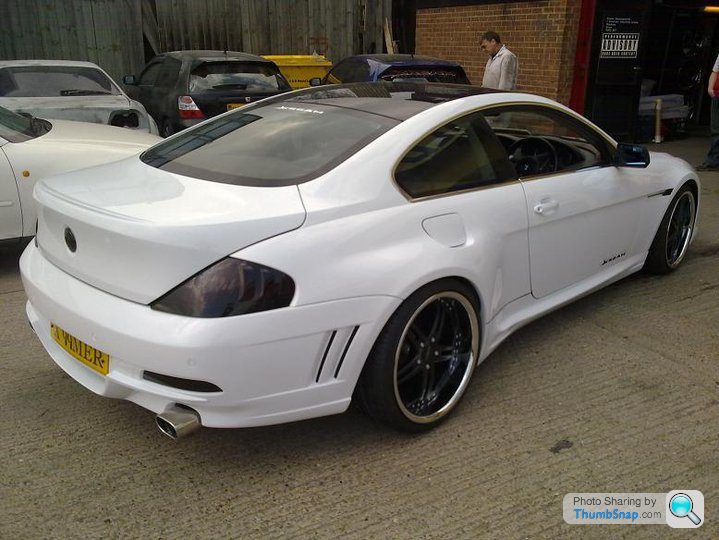 Badly modified cars thread - Page 134 - General Gassing - PistonHeads - The image displays a white sports car parked outdoors, likely in a car lot or a similar environment. The car is a two-door model, with a clean and well-maintained appearance. The vehicle's design includes a short, rear-sloping roofline, and it features a set of five-spoke alloy wheels. The background of the photograph shows several other cars parked in the same area, with at least one person, possibly a bystander, visible in the distance.