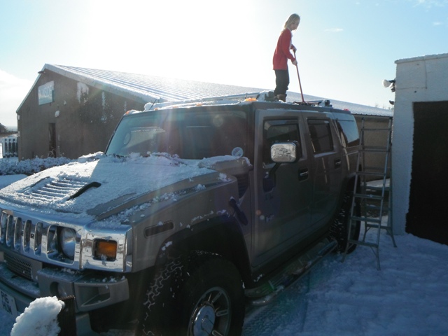 The official 2012/2013 snow thread - Page 348 - The Lounge - PistonHeads - The image showcases a young boy engaged in a playful activity on top of a large, snow-covered SUV. He appears to be using a broom or similar object to perform some sort of removal or cleaning on the car. The SUV itself is a four-door model with black accents, indicating it might be a specialized model designed for sturdy products. The location seems to be a street or driveway, as the presence of a house with a brown roof in the background suggests. The sun shines brightly over the scene, casting a warm glow on the snow, enhancing the overall feeling of a cold but sunny day.