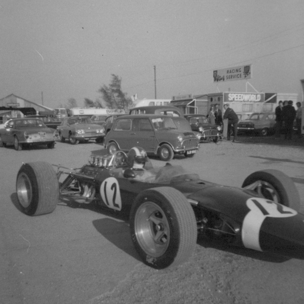 Fantastic Motorsport Photos! - Page 156 - General Motorsport - PistonHeads - The image features a vintage race car, numbered 12, with a prominent black color and white stripes on the body and nose. It appears to be a Formula 1 car. The setting is a gravel lot, and the car is displayed outdoors, possibly on a test track. In the background, there are several older cars and trucks, as well as a garment Suzuki sign, suggesting that the scene may be related to automotive history or a specific racing event.