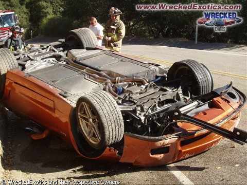 A red motorcycle parked in a parking lot - Pistonheads - The image captures a scene of a wrecked car that has tipped over onto a grassy area. The car, which is prominently orange, has sustained significant damage, with parts appearing mangled and broken. Two individuals wearing fire department uniforms, complete with helmets, are seen attending to the incident, possibly assessing the damage or trying to stabilize the vehicle. The background features a clear sky and slightly distant view of a sign labeled "wreckedExotics.com," perhaps indicating the location or program of the event involving the damaged car. The image conveys the aftermath of a crash incident with emergency personnel onsite.