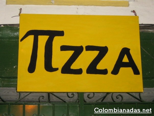 The image features a yellow signboard with the word "TZZA" in large, bold, black letters. The signboard is hanging outside a building, with its back side facing the viewer. The background appears to be an outdoor setting, as evidenced by a colorful wall that forms a part of the building where the signboard is mounted.