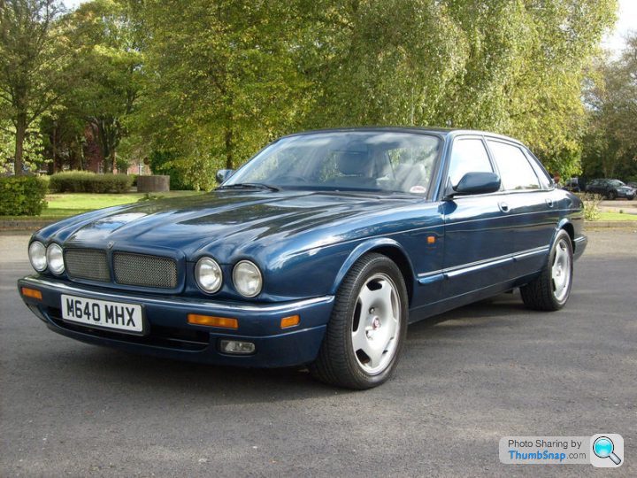 A black and white photo of a car parked in a parking lot - Pistonheads - The image showcases a blue Jaguar car with the registration number M640 WHX prominently displayed on its front bumper. The vehicle is parked on an asphalt surface, viewed from a slightly elevated position that allows a clear view of its front and side profile. It exhibits a well-maintained quality with shiny exterior paint and clean, functional-looking alloy wheels. The car is surrounded by a natural setting, with trees and grass visible, suggesting that it's parked in a parking lot or a similar outdoor environment.