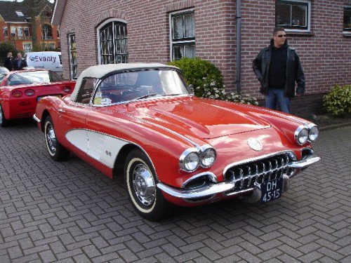 C1 Corvette stolen from Corvette Fame Meeting - Page 1 - Corvettes - PistonHeads - The image captures a classic red Cadillac convertible car parked on a brick driveway in front of a building. The car has a convertible top down, revealing a shiny interior. Near the car, there is a man standing to the right, observing the vehicle. In the background, you can see another car on the street, partially obscured by the red Cadillac. The brick driveway and the building suggest an urban or residential setting.