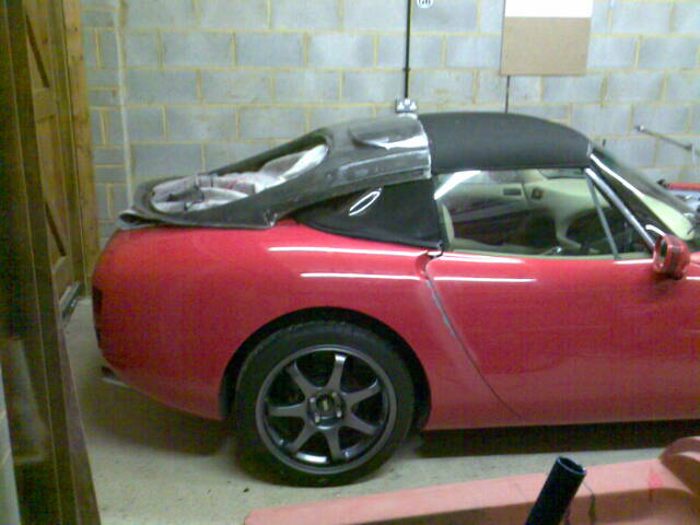 GT style racer hard top - Page 1 - Major Mods - PistonHeads - The image shows a red sports car parked indoors, with its engine compartment open. A black fabric covers the open engine bay. Above the engine, a pair of boots is casually propped, indicating a possible recent arrival of the car's occupant. The car has black rims and a sleek design typical of sports cars. The setting appears to be a garage or indoor storage area with concrete walls in the background.