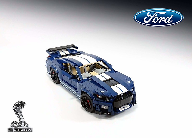 Non Technic LEGO - Page 271 - Scale Models - PistonHeads - The image shows a toy replica of a Ford Mustang. It is painted in shades of blue and white, with the hood appearing to be open. The car has visible details such as a stripe running down its side, black tires, and a spoiler on the rear. In the background, there's a logo that reads "FORD" and another smaller text that appears to be a brand or model name. The overall style of the image is clear and focused, with a high-contrast lighting effect that highlights the car's details and colors.