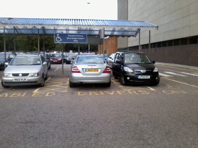 The BAD PARKING thread - Page 517 - General Gassing - PistonHeads - The image shows a parking lot with several cars. There are parking spots designated for disabled and blue badge holders, as indicated by the signage. The cars are parked in a way that they block the image, showing only their backs, and they occupy multiple spots. The environment appears to be a typical public parking area. The image has a clear focus, and the cars are in good condition, suggesting recent use.