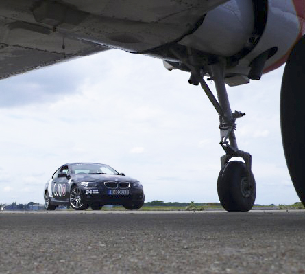 Your Car Stickered Up For Le Mans 2010! - Page 29 - Le Mans - PistonHeads - The image captures a rather unusual scene: a car is positioned directly beneath a large airplane wing. The airplane is white and is parked on a tarmac. The car, being the foreground of the image, is largely in focus, and it appears to be a model Bmw, as evidenced by its distinctive design and branding. The text visible on the car reads "FOR 9," indicating it might be a rental vehicle, and "Bavaria Bmw," suggesting the model or make of the car. The image is well-composed, with the car and plane wing as the two key elements. The tarmac around them is smooth and gray, and the sky above is colored with hues of blue and gray, suggesting it might be an overcast day. The interaction between the car and the airplane wing is intriguing and could be seen as symbolic of the juxtaposition of ground travel and air travel.