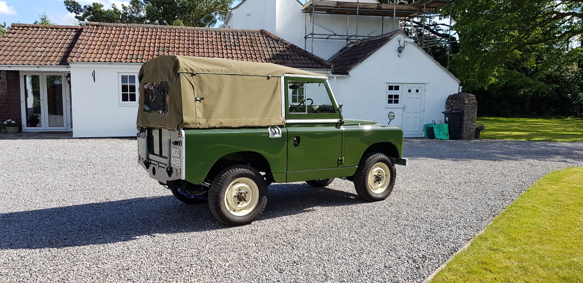 show us your land rover - Page 102 - Land Rover - PistonHeads - The image depicts a scene in a driveway. A vintage green Land Rover is parked prominently in the center of the frame. It has an old-fashioned look, reminiscent of army transport vehicles from past decades. Behind the Land Rover, there's a gravel area leading up to a house with a white exterior and a chimney on its roof. The house is partially obscured by the vehicle. To the left of the Land Rover, there are several stone steps leading down to the driveway. The sky appears to be overcast, suggesting it might be an early morning or late afternoon time.