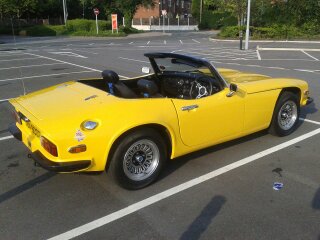 Hi from a newbie 3000S owner - Page 1 - Classics - PistonHeads - The image shows a bright yellow sports car parked in a large parking lot. The car is shiny and appears to be well-maintained. There are no visible passengers inside the car. In the background, there's a tree line and some vehicles are also parked nearby. The car is positioned facing the camera, offering a clear view of its front and part of the side. The lighting suggests it might be early morning or late afternoon, given the soft and diffused light.