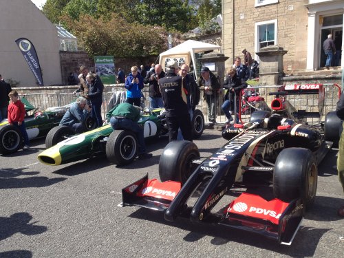 A group of people standing around a motorcycle - Pistonheads - In the image, a group of men are gathered around three colorful race cars parked on a street. The cars are painted in vibrant shades of green and red, each bearing the mark of a sponsor. One car is positioned in the foreground, with the other two parked behind. The men present vary in age and attire, attesting to the diversity of the audience. They appear to be in the midst of conversation, perhaps discussing the cars or sharing a memorable moment from the event. The background features a quaint brick building and a stone fountain, giving the scene a charming, old-world feel.