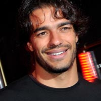 Namoitadobbb - The image is a close-up headshot of a man smiling at the camera. He has a beard and dark curly hair. The background is blurred but appears to be a dimly lit environment. There are no visible texts or logos in the image. The style of the image is a portrait, likely intended for promotional or personal professional use.