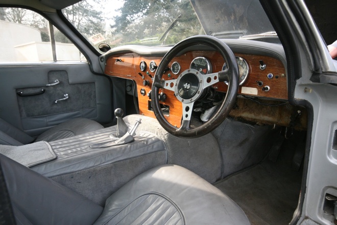 Early TVR Pictures - Page 35 - Classics - PistonHeads - The image shows the interior of a vintage car, focusing on the driver's side. The cabin features gray upholstery, with a distinctive wooden dash panel. A matching wooden steering wheel is at the center of the frame, adorned with various car electrics and dials. The settings appear to be mechanical and automatic, as suggested by the old-fashioned dashboard with many controls and gauges. The gear shift lever is prominent, indicating a manual transmission. The seating appears to be comfortable and simplistic, in keeping with the overall vintage aesthetic of the car's interior.