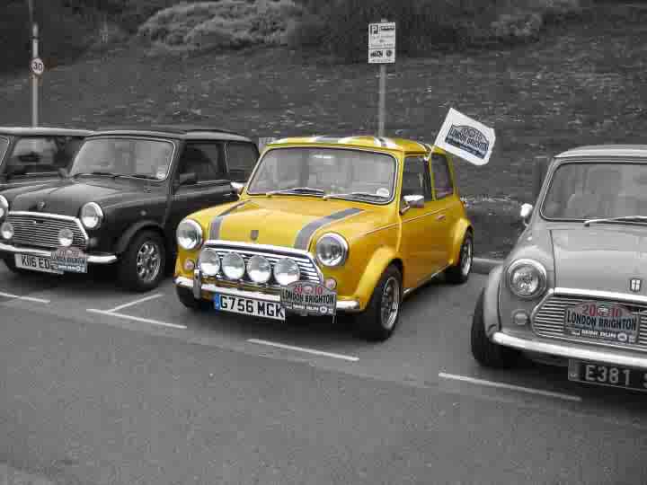 Fancy selling me your mini - Page 1 - Classic Minis - PistonHeads - The image portrays an alignment of three classic cars, each with a unique color and distinctive features, parked side by side in a parking lot. The first car is a black Mini Cooper Cooper S with a striking dark stripe, the second is a yellow Mini Cooper S model, and the third is a silver Mini Cooper Cooper S. Each car displays a special edition badge, and the black car is equipped with a roof rack, while the mini Cooper Cooper S model has flags on the front. The cars are parked next to a sign, suggesting they're part of an event or gathering. All cars appear to be in good condition, with shiny surfaces reflecting the overcast sky.