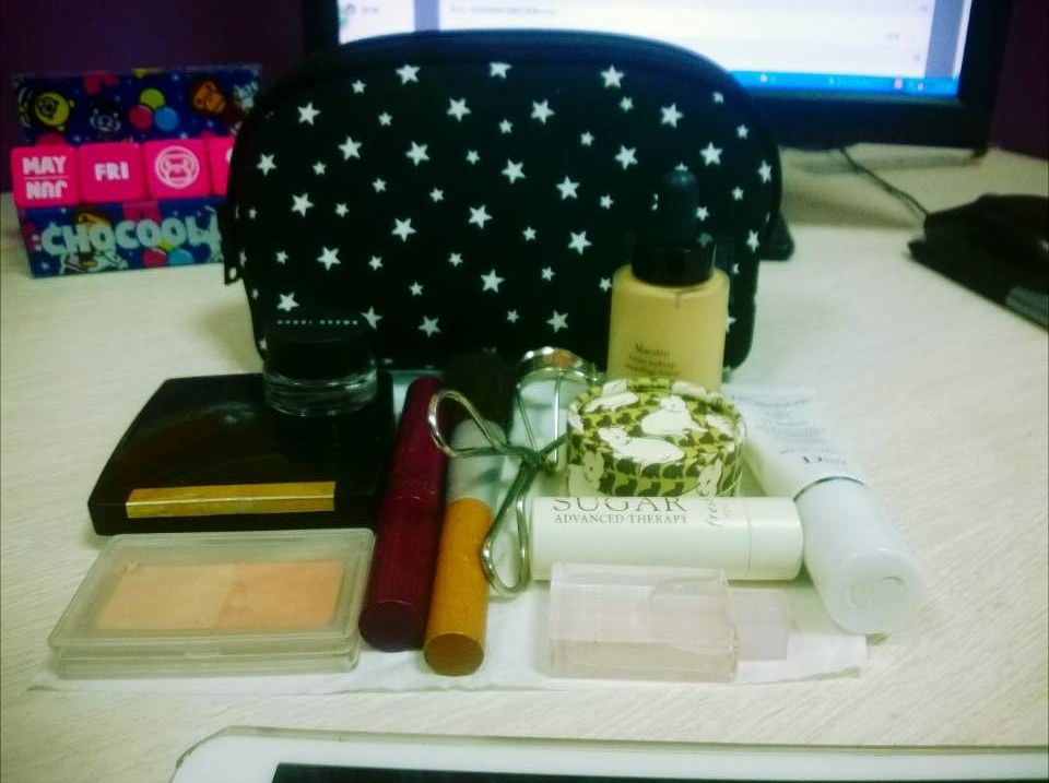 A table topped with a laptop and a smart phone - The image shows a collection of various cosmetic items arranged on a countertop. There's a blue makeup bag with a black star pattern in the middle of the image. To its left, there's a purple and white packaging next to a clear box containing what appears to be a blush or bronzer. To the right of the bag, there are several items including a toothbrush, a small container, and a pair of scissors with a red handle. In the foreground on the left side, there is a small, black device resembling a cell phone. To the right, on the floor, there's a white shoe. Overall, it seems to be a collection of items often found in a personal care or makeup bag.