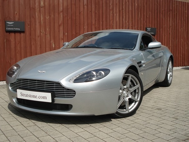 Owner Guys Pistonheads - The image shows a sleek, silver sports car parked on a brick pavement. The vehicle is positioned at an angle to the viewer, allowing a clear view of its front and side. The car has a distinctive design with a large grille and angular headlights. There is a license plate affixed at the front of the vehicle. The background features a wooden structure wall, providing a contrasting texture to the smooth finish of the car. The car is advertised as a Stratstone.com vehicle, suggesting it may be for sale or rent.